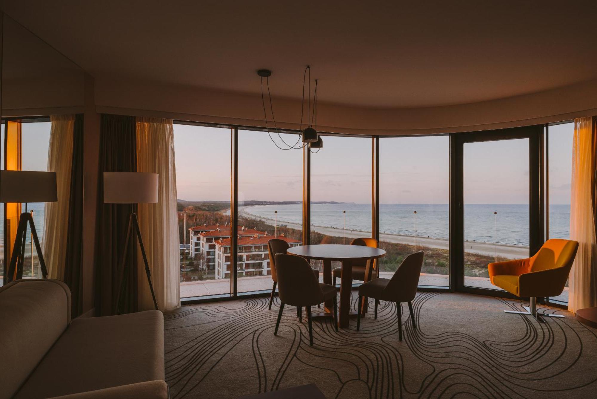 Radisson Blu Resort Świnoujście Exterior foto The photo shows a modern and stylish interior of a room featuring large windows that provide a view of the beach and ocean. The room is furnished with a round table and chairs, along with a cozy sofa and a bright yellow armchair. The decor has a cont