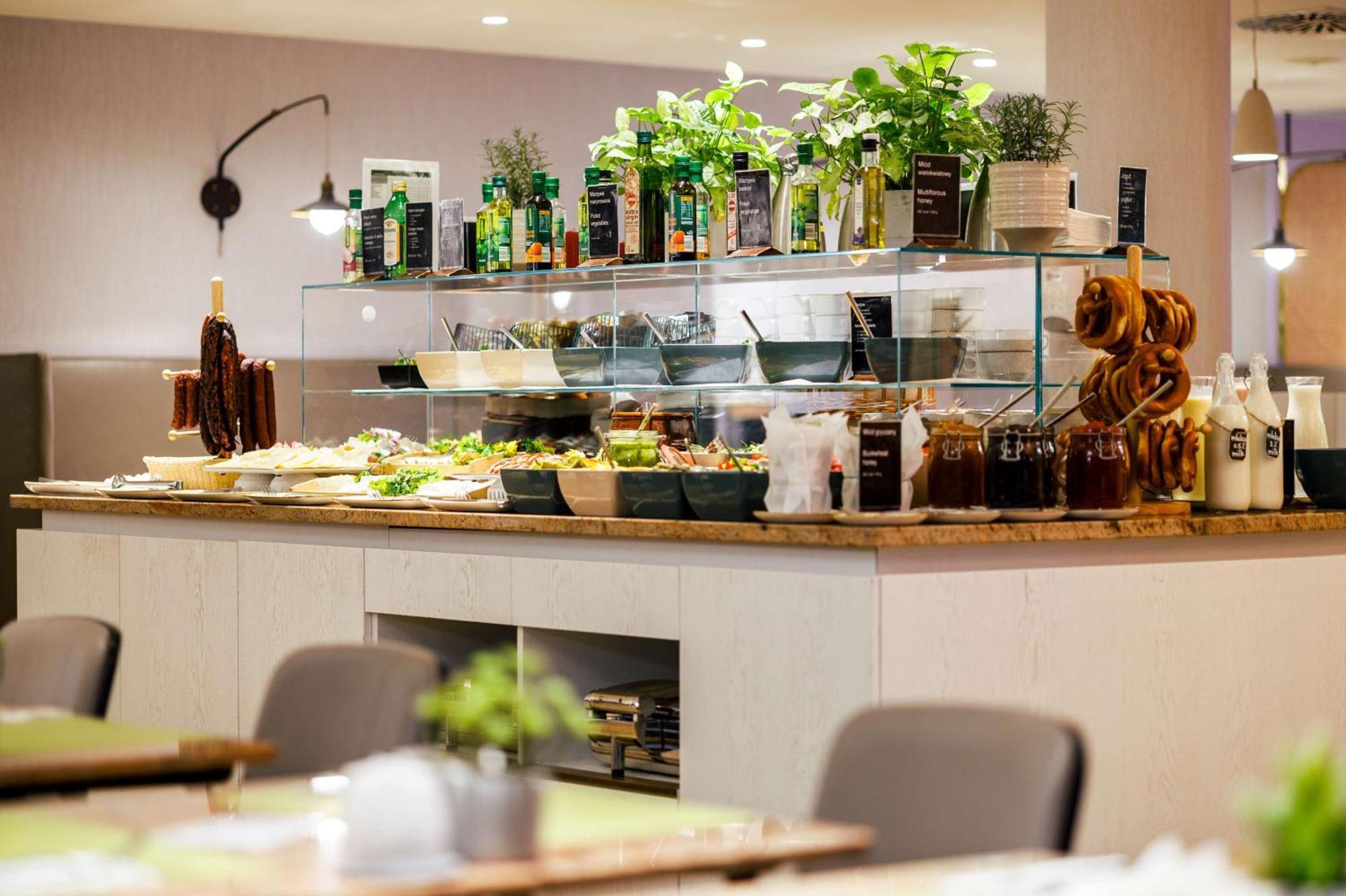 Radisson Blu Resort Świnoujście Exterior foto The photo shows a well-organized buffet display in a restaurant setting. There is a glass counter filled with various dishes. On the upper shelf, there are several bottles of oil and herbs, indicating a focus on fresh and healthy ingredients. Below t