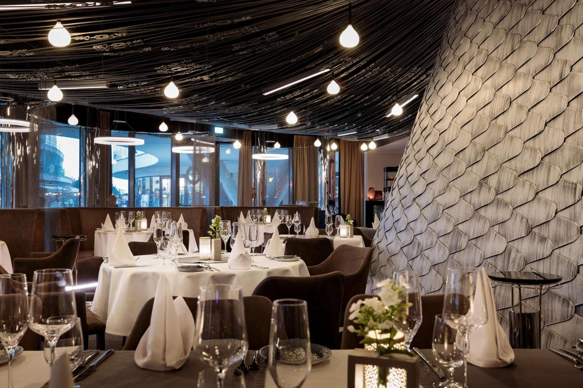 Radisson Blu Resort Świnoujście Exterior foto The photo shows a stylish restaurant interior. The dining area features elegantly set tables with white tablecloths, glassware, and folded napkins. There are decorative elements like small floral arrangements on the tables. The ceiling is adorned wit