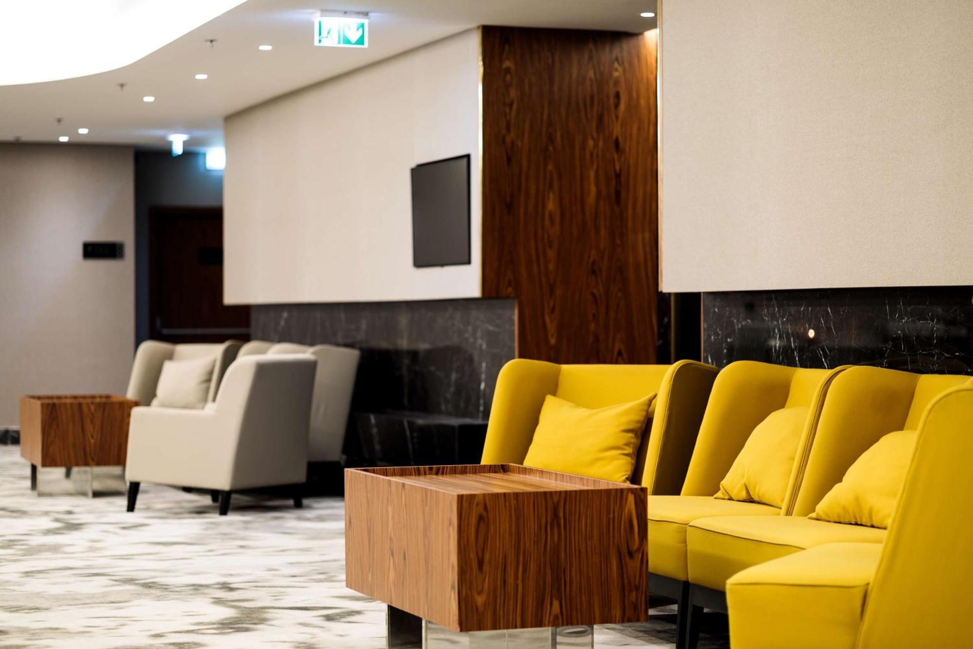 Radisson Blu Resort Świnoujście Exterior foto The photo depicts a modern lounge or waiting area with stylish seating. On the left, there are soft gray armchairs arranged around a wooden coffee table. In the center, there are yellow chairs with plush cushions, contributing a vibrant contrast to t