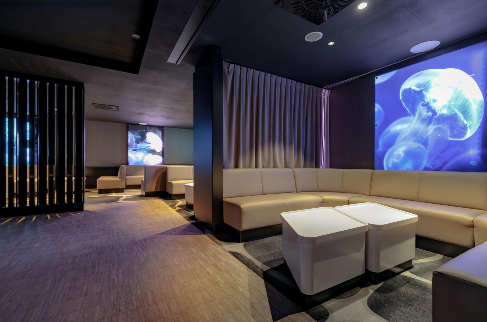 Radisson Blu Resort Świnoujście Exterior foto The photo shows a modern interior space that appears to be a lounge or relaxation area. The design is sleek and minimalist, featuring a curved, light-colored seating arrangement with low tables at the center. The walls are dark, contributing to a coz