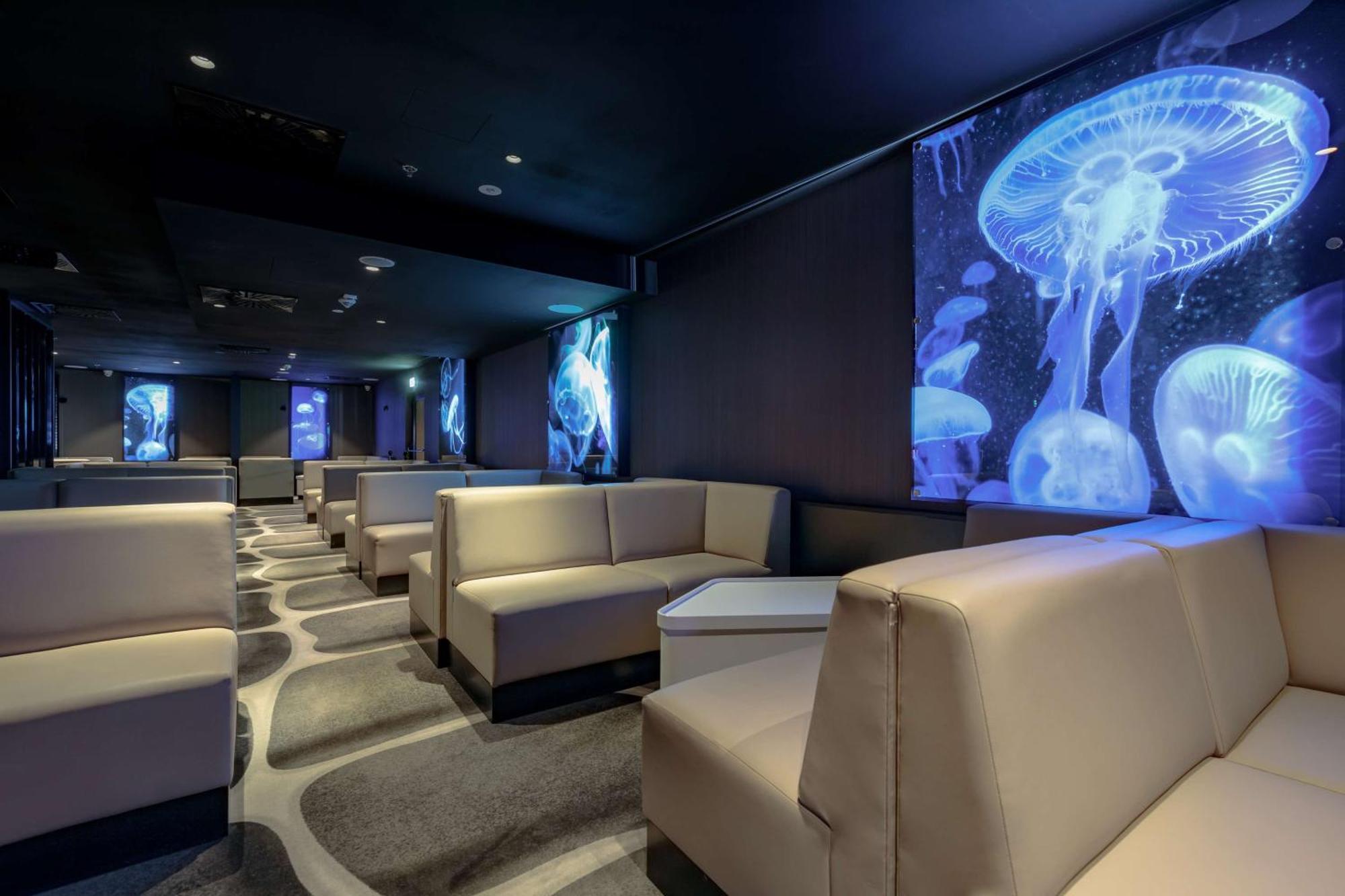 Radisson Blu Resort Świnoujście Exterior foto The photo shows a modern lounge space with a sleek design. The area features light-colored, upholstered seating arranged in an open layout. The walls are decorated with large, vibrant images of jellyfish illuminated in blue, creating a calming underw
