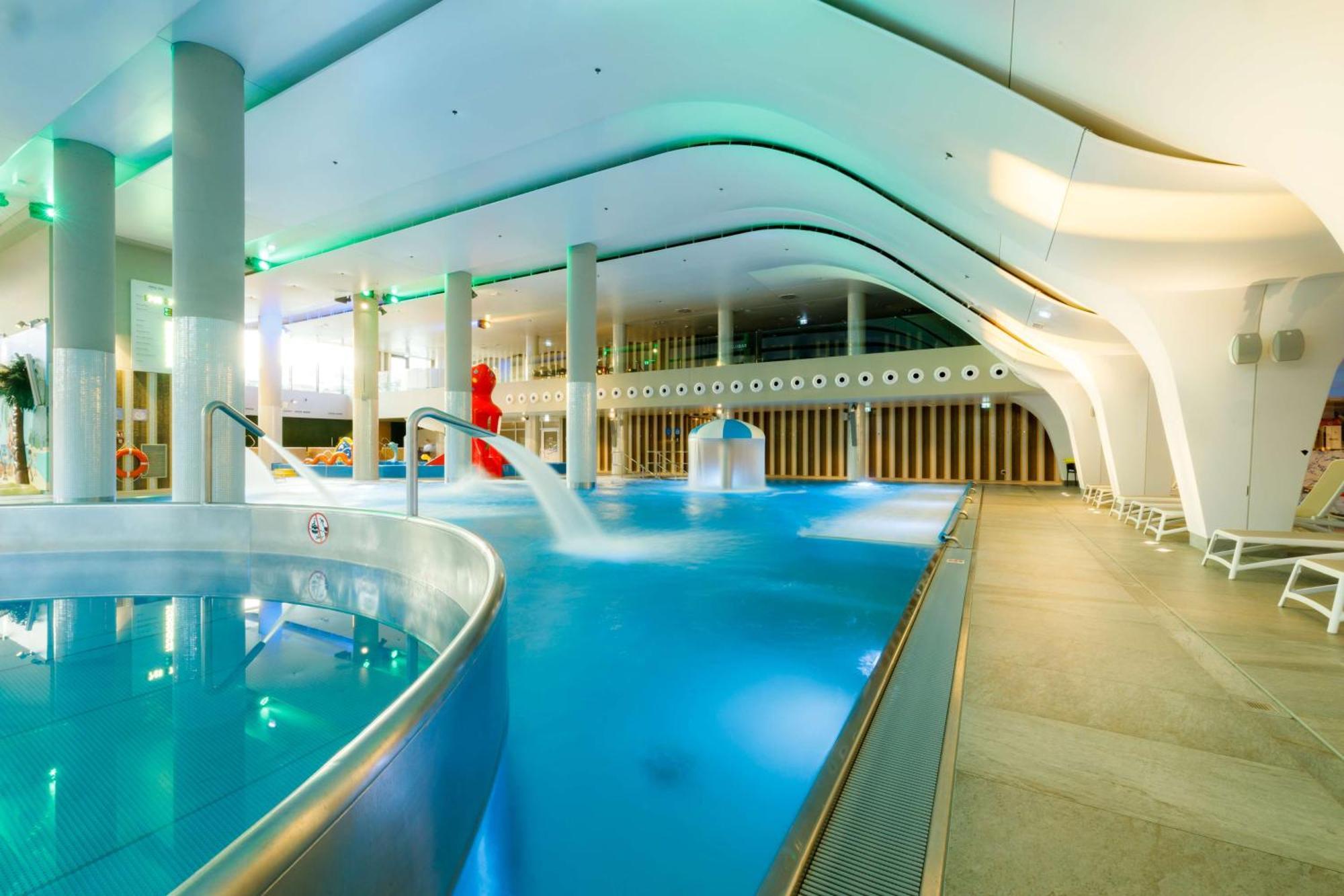 Radisson Blu Resort Świnoujście Exterior foto The photo shows a modern indoor swimming pool area with an elegant design. The pool features curved edges and is filled with clear, blue water. There are various amenities, such as jets for relaxation and possibly seating areas along the edges. The l