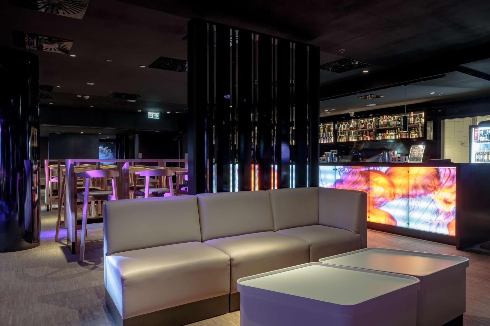 Radisson Blu Resort Świnoujście Exterior foto The photo depicts a modern interior space, possibly a lounge or bar. There are sleek, minimalistic furniture pieces, including a large, curved sofa and contemporary coffee tables. The lighting is dim, with a blend of colorful ambient lights illuminat