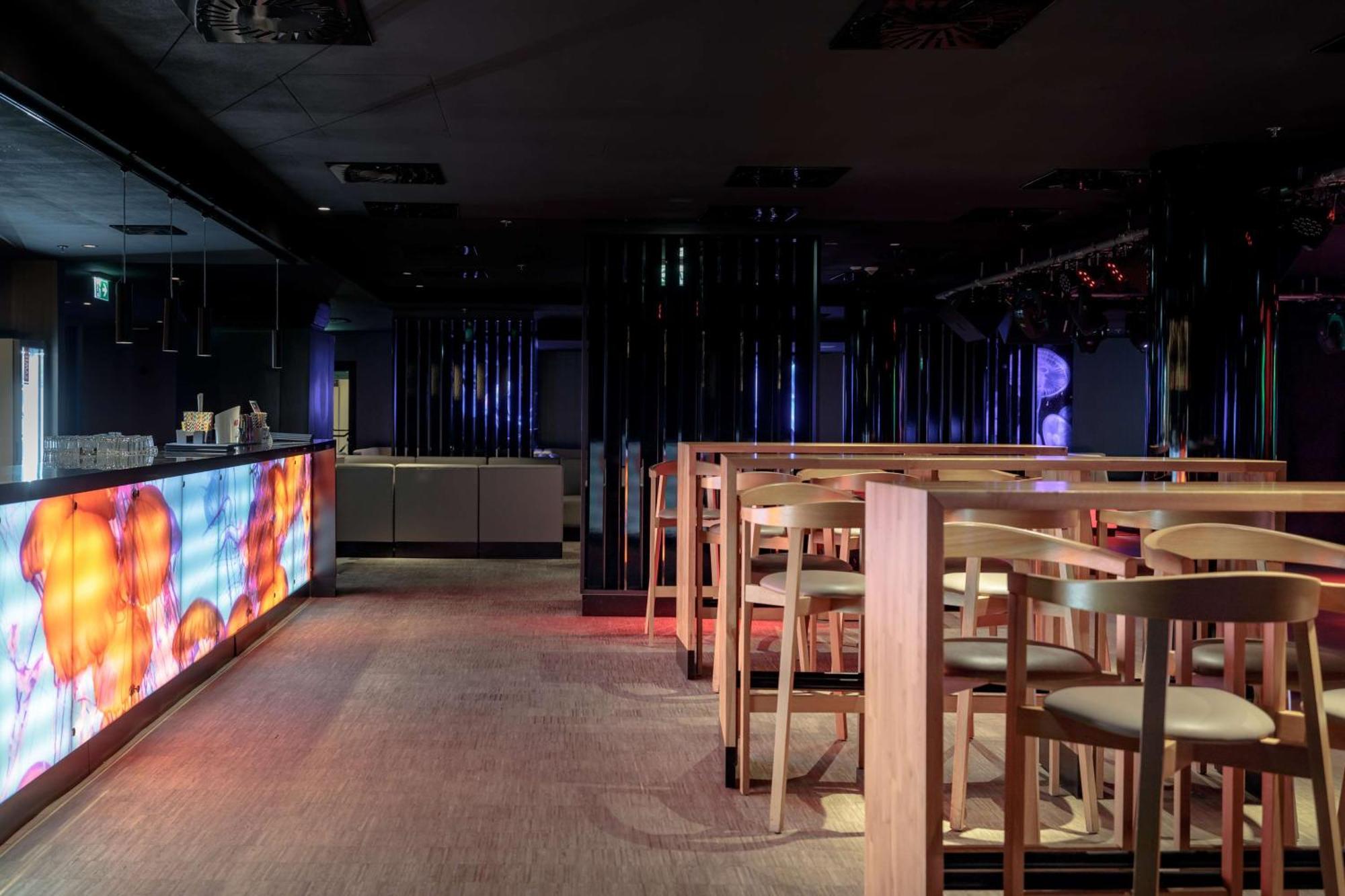 Radisson Blu Resort Świnoujście Exterior foto The photo shows the interior of a modern bar or nightclub. It features a sleek and stylish design with a long bar counter illuminated by colorful lights. The floor has a neutral carpet, and there are wooden high-top tables with accompanying chairs ar