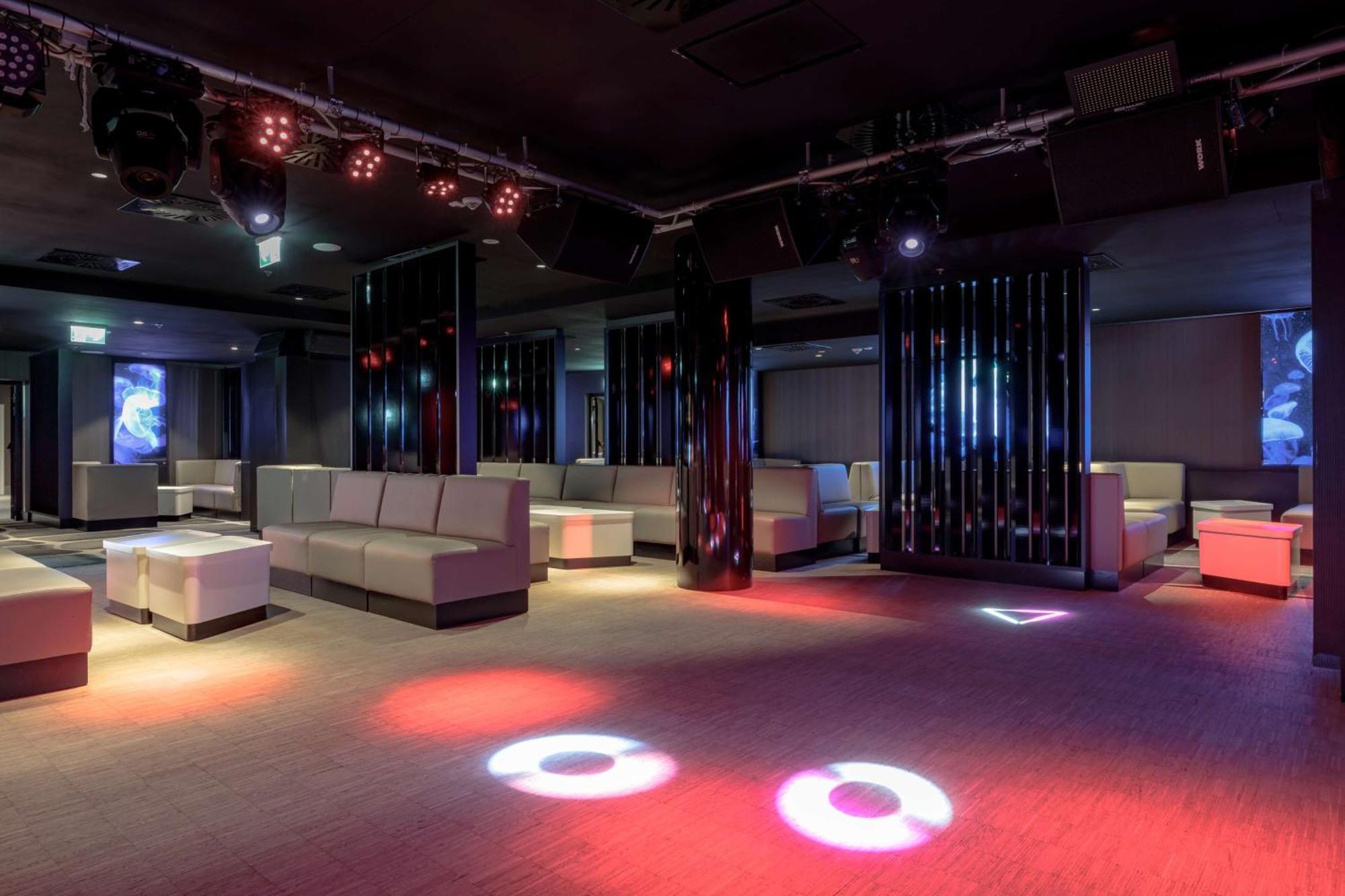 Radisson Blu Resort Świnoujście Exterior foto The photo depicts a modern nightclub interior, featuring a spacious layout with sleek, minimalist seating arrangements. The room has plush seating along the walls, and the floor is illuminated with circular lights in varying colors, creating a vibran