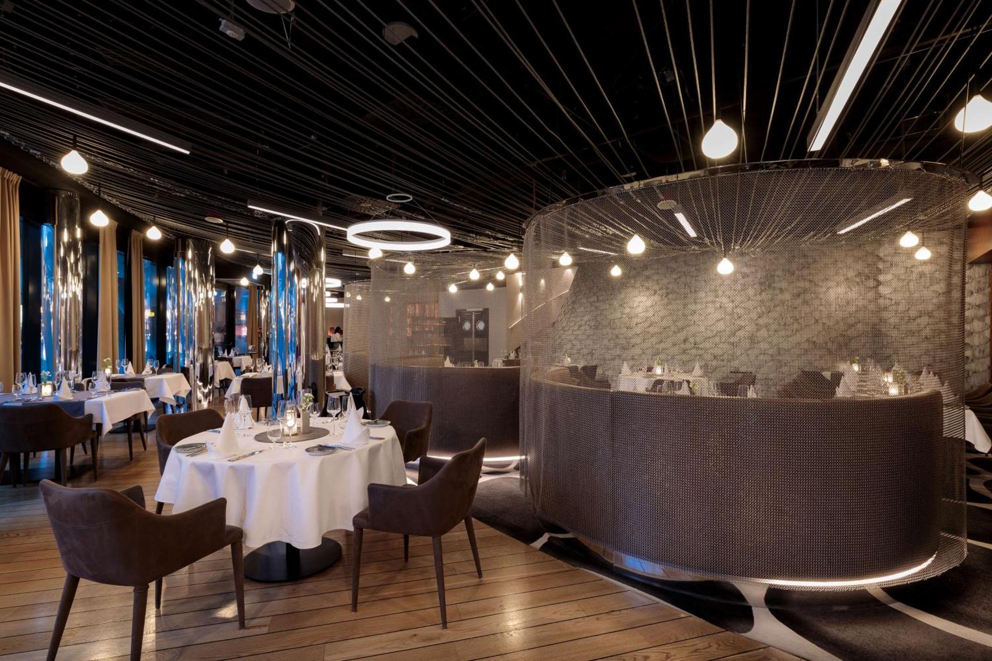 Radisson Blu Resort Świnoujście Exterior foto The photo shows an elegant restaurant interior. It features polished wooden floors and contemporary decor. Round tables are set with white tablecloths and have chairs arranged around them. The lighting is modern, with multiple pendant lights hanging 