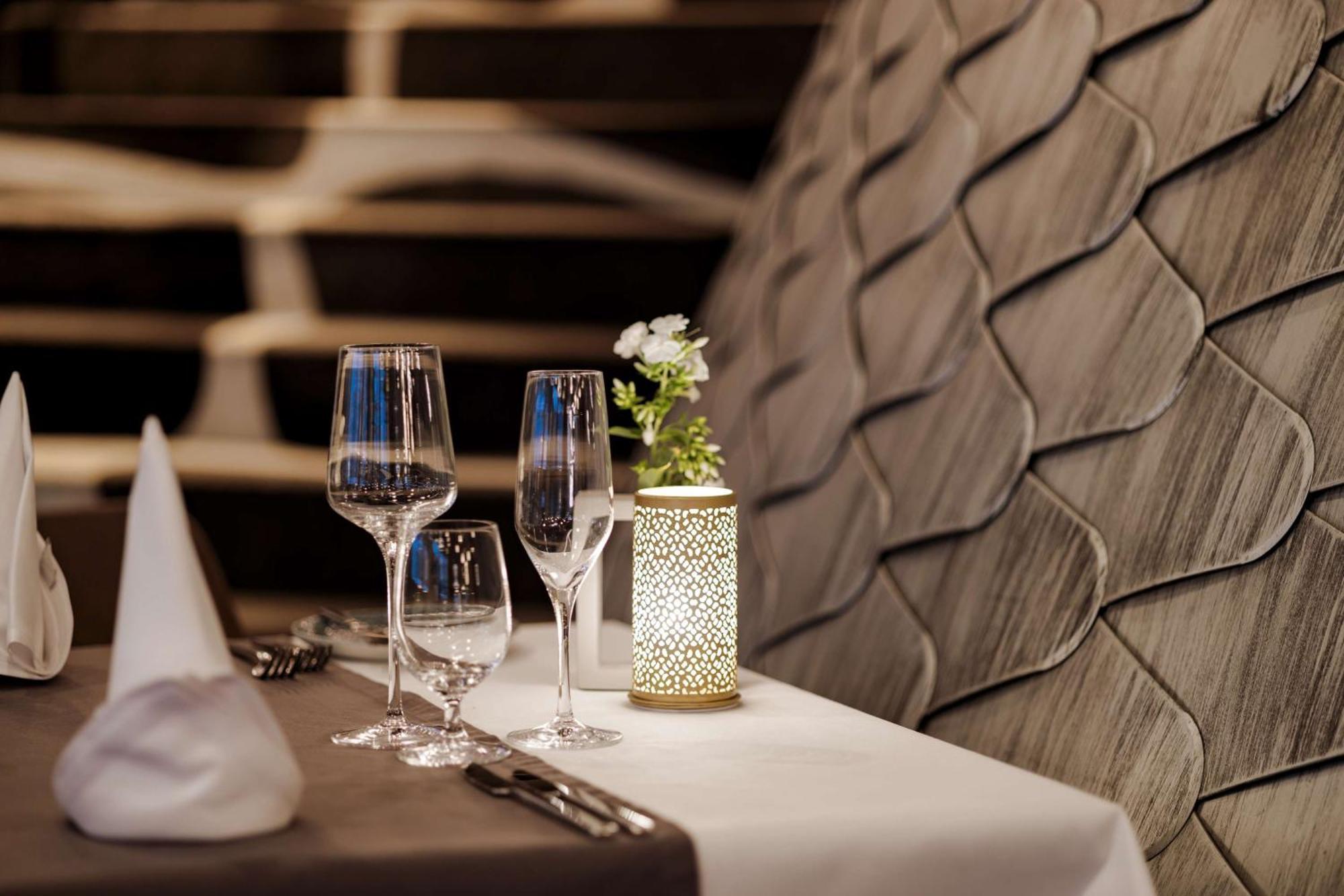 Radisson Blu Resort Świnoujście Exterior foto The photo shows a beautifully arranged table setting in a restaurant. There are two elegant wine glasses and a smaller glass, likely for water, placed on a crisp white tablecloth. A decorative lantern with intricate designs holds a small flower arran