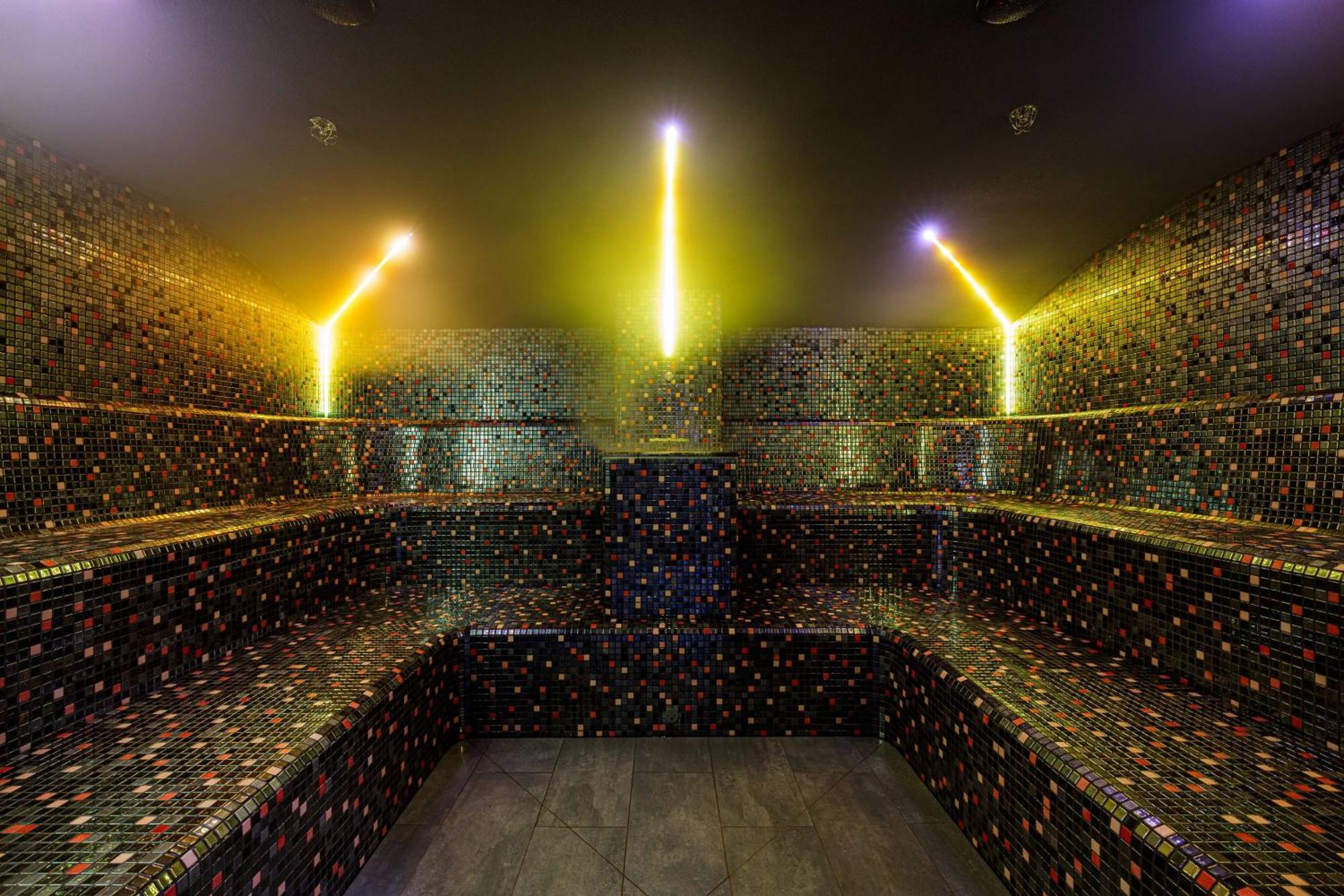 Radisson Blu Resort Świnoujście Exterior foto The photo shows the interior of a steam room or sauna. The space is characterized by a series of benches that are built into the walls, allowing for multiple seating options. The walls are adorned with a mosaic of small, colorful tiles that create a 