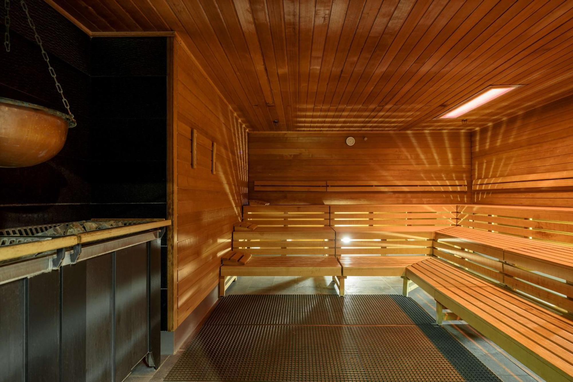 Radisson Blu Resort Świnoujście Exterior foto The photo shows the interior of a sauna. The walls and benches are made of wood, creating a warm and inviting atmosphere. There is a heater, likely for generating steam, and a metal rack connected to it, perhaps for holding stones or water. The desig