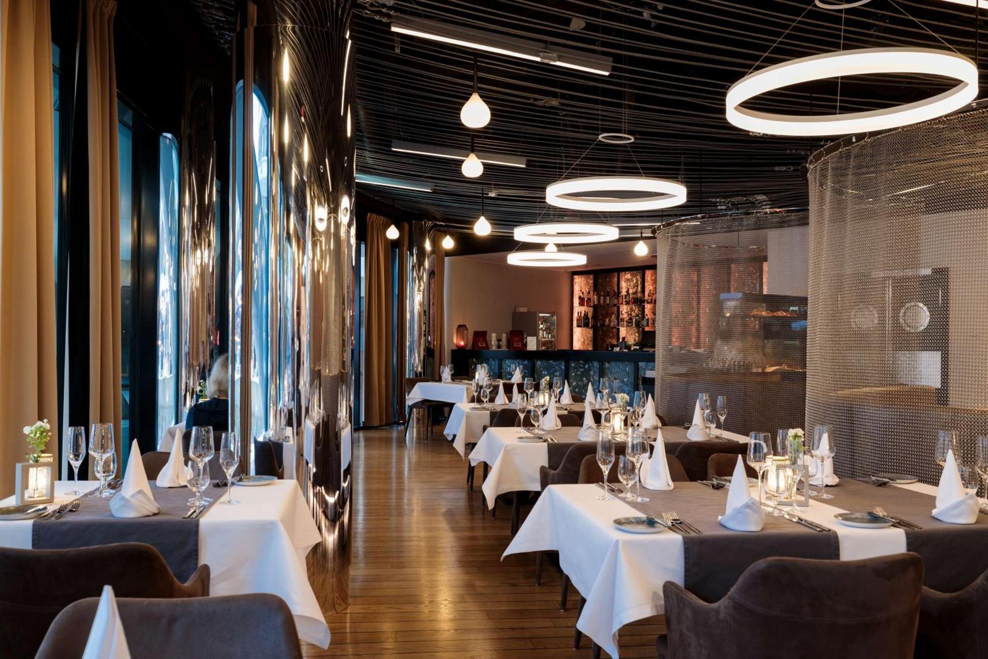 Radisson Blu Resort Świnoujście Exterior foto The photo shows the interior of a modern restaurant. It features elegantly set tables with white tablecloths and neatly arranged glassware. The design includes a sleek, contemporary aesthetic with dark walls and interesting lighting, including circul