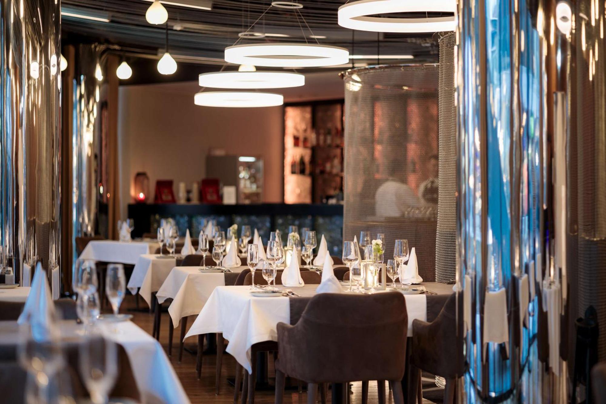 Radisson Blu Resort Świnoujście Exterior foto The photo depicts an elegant restaurant interior. There are several tables covered with white tablecloths, each set with glassware and napkins, suggesting a fine dining experience. The chairs are upholstered, providing a comfortable seating arrangeme