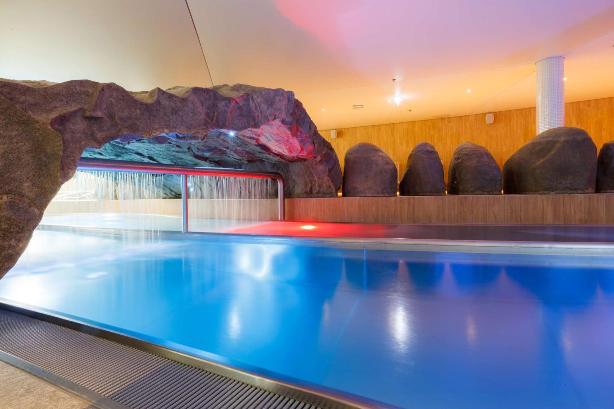 Radisson Blu Resort Świnoujście Exterior foto The photo shows a serene indoor swimming pool area. The pool has clear blue water, and there is a distinctive rock formation that resembles a cave on one side. Soft lighting enhances the atmosphere, casting a gentle glow across the space. In the back