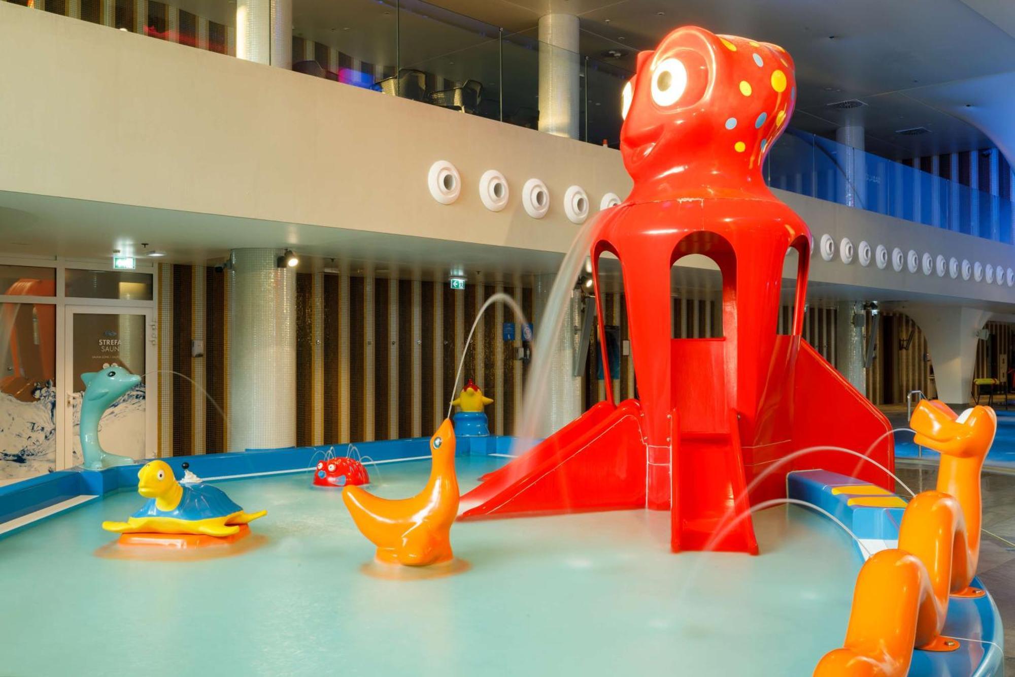 Radisson Blu Resort Świnoujście Exterior foto The photo shows a colorful indoor splash pad or water play area designed for children. Central to the scene is a large, bright red octopus structure, which has water fountains spraying out. Surrounding it are various playful, colorful water animals, 